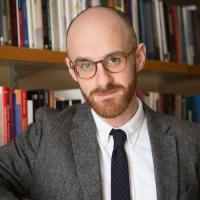 Alexander Livingston poses in front of a full bookshelf wearing orange-framed glasses